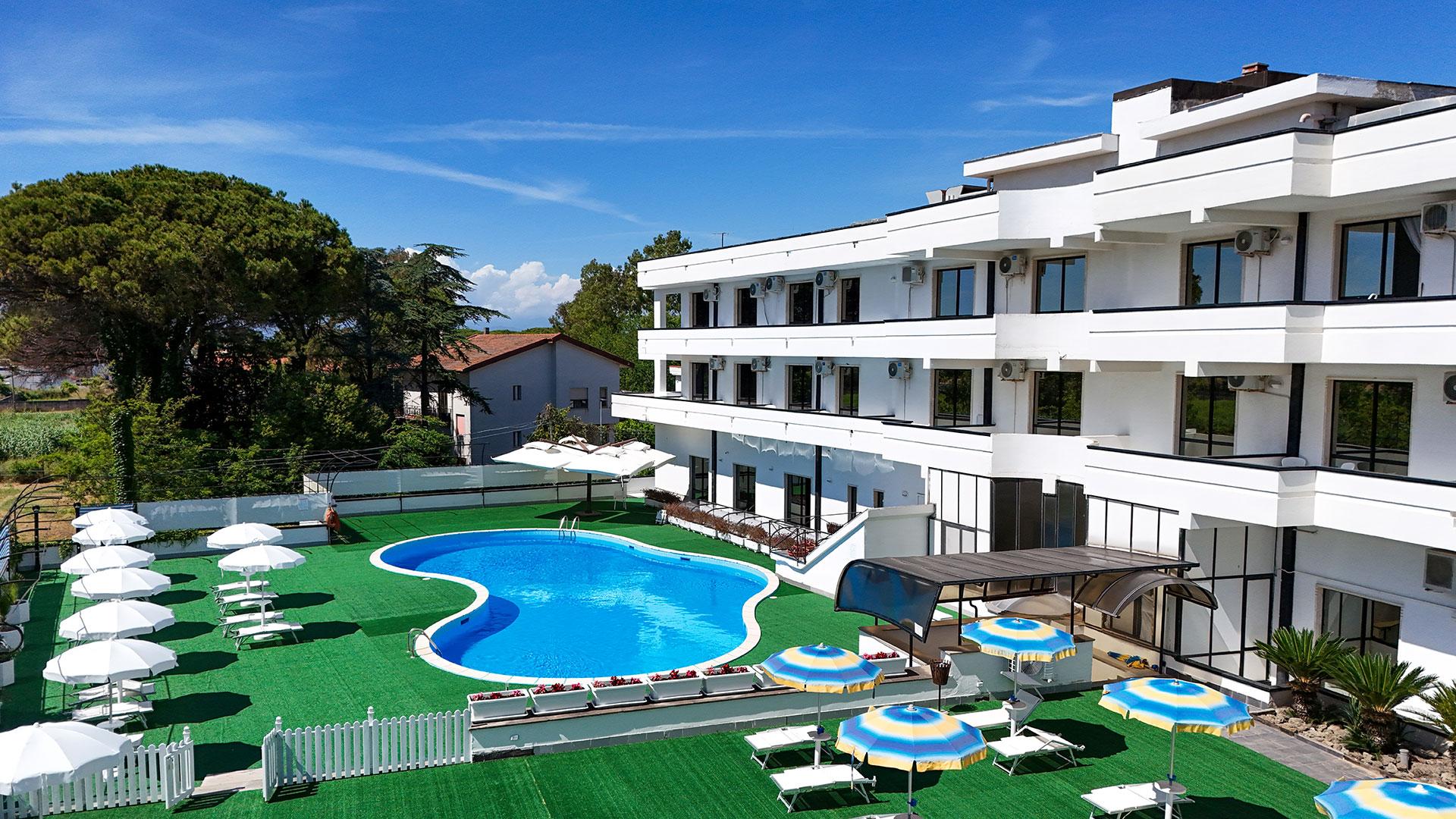 Hotel moderno con piscina, ombrelloni e lettini su prato verde.