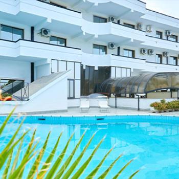 Moderno hotel con piscina, terrazze e ampie finestre, circondato da vegetazione.