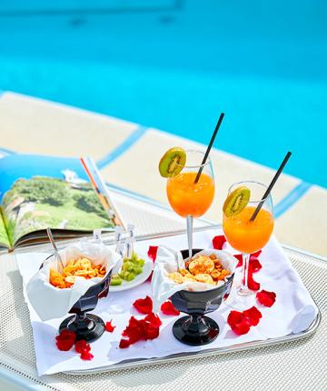 Cocktail e snack a bordo piscina con petali di rosa e rivista aperta.