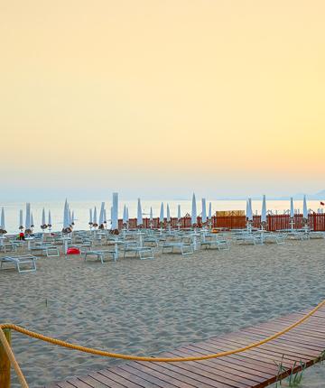 Spiaggia al tramonto con lettini e ombrelloni chiusi, atmosfera tranquilla e serena.