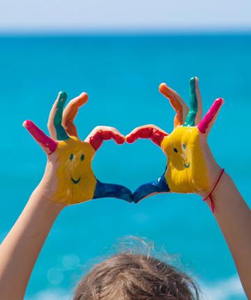 Mani dipinte con sorrisi e colori vivaci, formano un cuore davanti al mare.