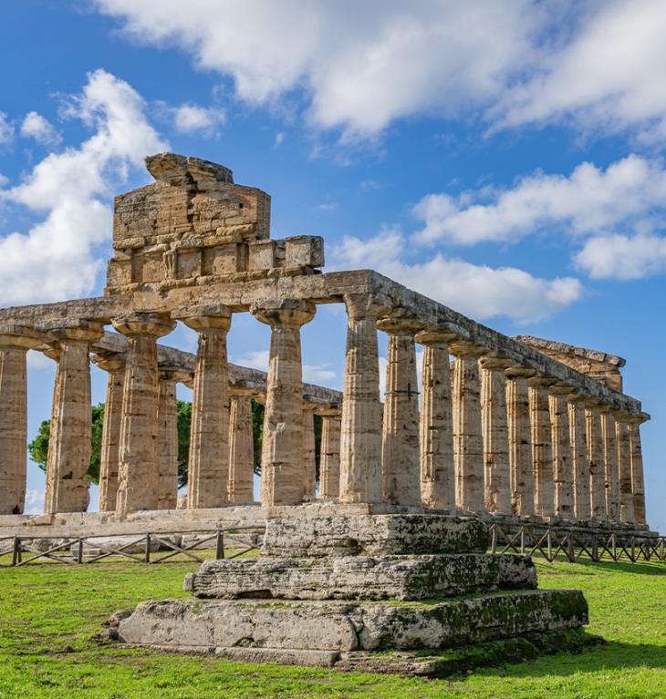 Tempio antico con colonne doriche, cielo blu e nuvole sullo sfondo.