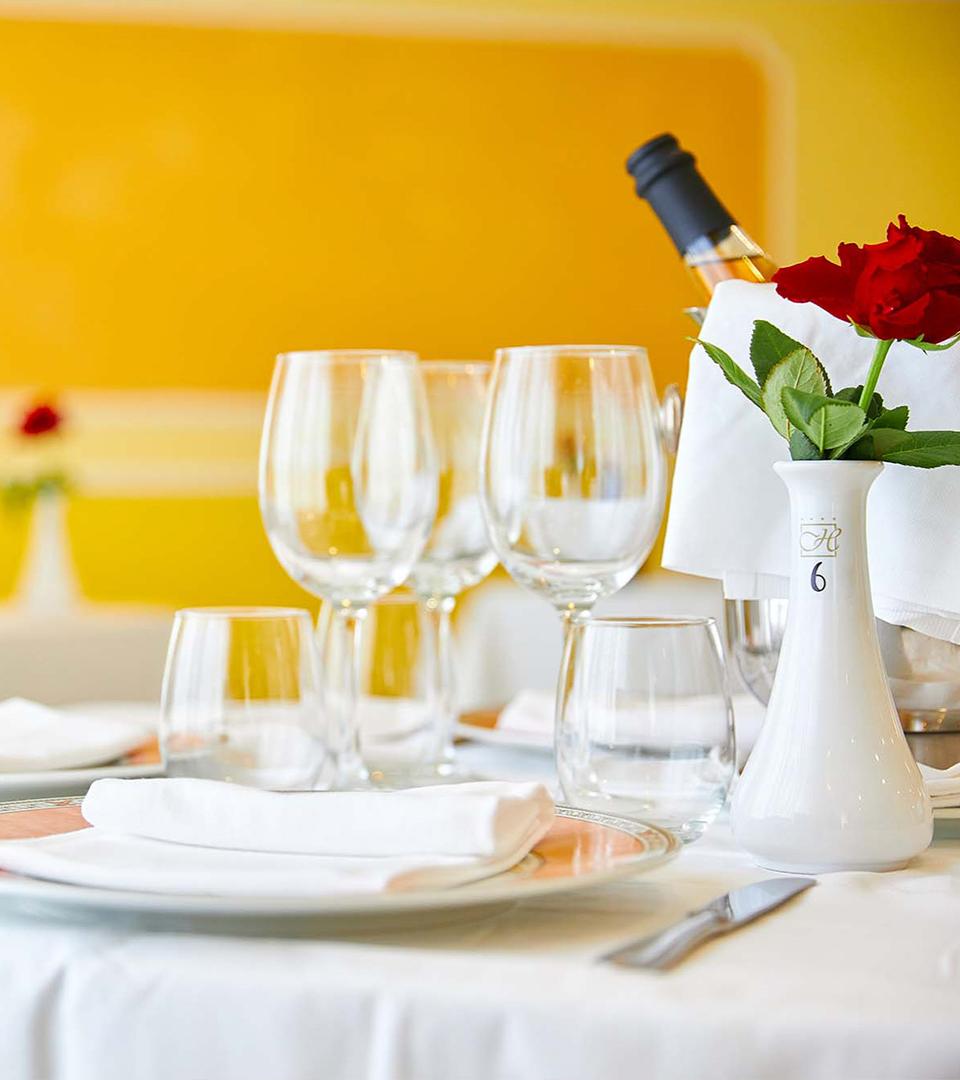 Tavolo elegante con bicchieri, piatti, tovaglioli e rosa rossa in vaso bianco.
