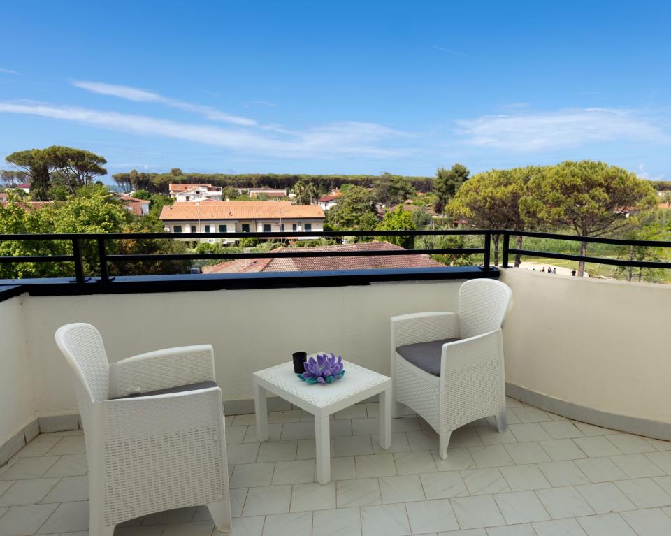 Terrazza soleggiata con sedie bianche, vista su tetti e alberi verdi.